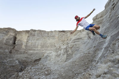 One man preforms a "wall ride" while trail running on a sandy terrain