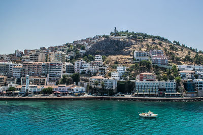 Sailboats in sea by buildings against clear sky