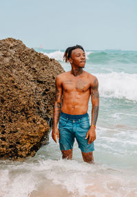 Full length of shirtless man standing at beach against sky