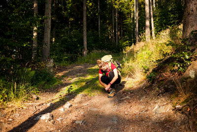 Full length of woman tying shoelace on footpath in forest