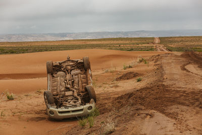 Damaged car in desert against sky