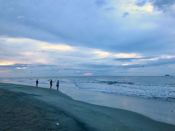 People at beach against sky during sunset