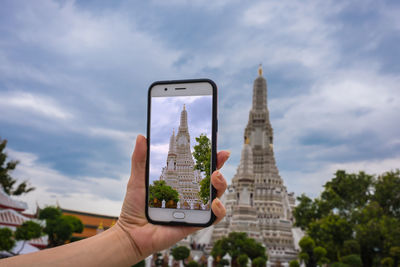 Hand holding smart phone against sky