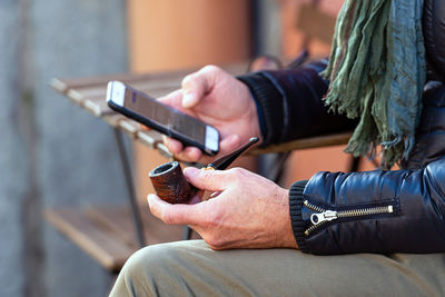 Midsection of woman using mobile phone while holding smoking pipe