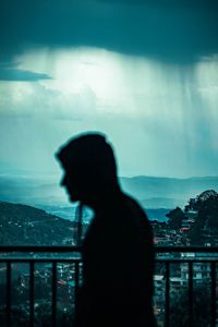 Silhouette man standing by railing against sky