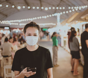 Front view young woman wear protection mask standing in night market , travel and recreation concept