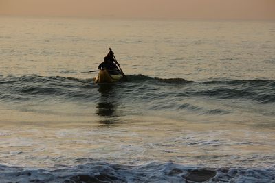 People in sea against sky during sunrise 