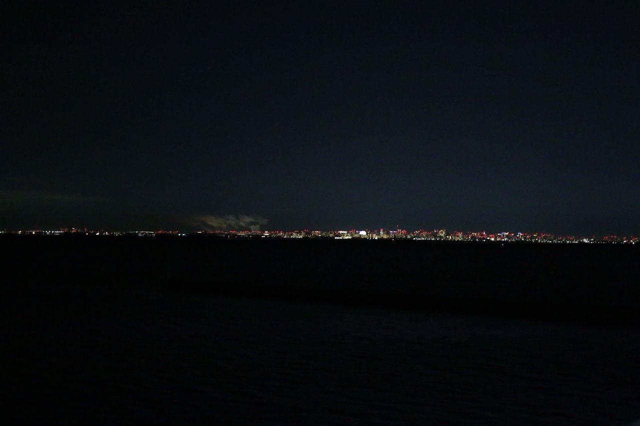 VIEW OF ILLUMINATED CITY BY SEA AGAINST SKY AT NIGHT