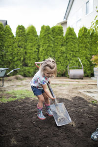 Two year old girl shoveling dirt in her backyard.