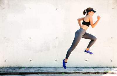 Full length of woman with arms raised against wall