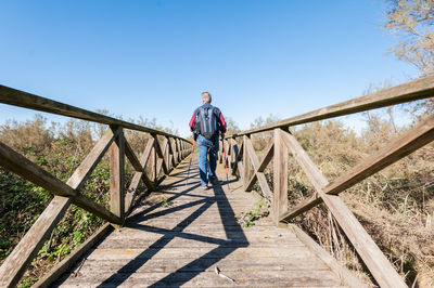 Man walking on footbridge against clear blue sky