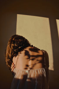 Rear view of woman standing against wall at home