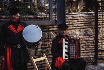 Men with instruments sitting on footpath in city