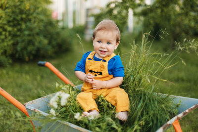 A charming baby sits in a wheelbarrow in the garden. summer outdoor activities for young children