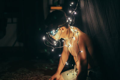 Illuminated string lights on side view of shirtless man sitting at home