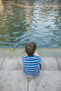 Rear view of boy sitting on water