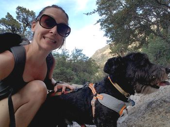 Portrait of smiling woman with dog sitting against trees