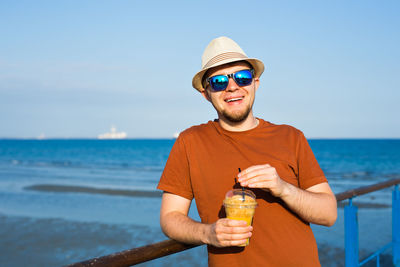 Young man drinking water from sunglasses against sea