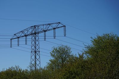 Low angle view of electricity pylon against clear blue sky