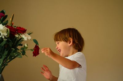Full length of boy holding flowers against wall
