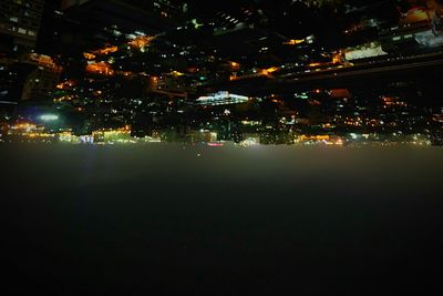 Illuminated city by sea against sky at night