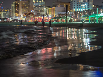 Illuminated buildings by river in city at night