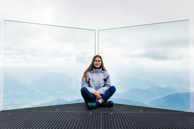 Portrait of young woman sitting on mountain against sky