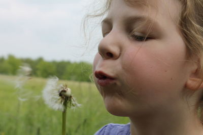 Close-up of girl blowing dandelion on field