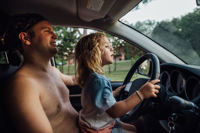 Daughter pretending to drive car on dads lap