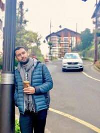 Portrait of man holding drink while standing by street light