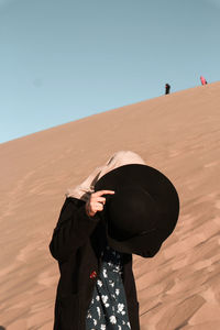 Person wearing hat standing on sand against clear sky