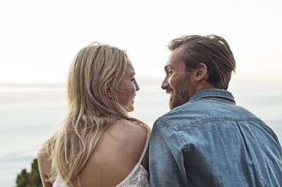 Rear view of happy couple looking at each other against clear sky