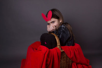 Portrait of smiling girl with costume rabbit ears sitting in basket against gray background