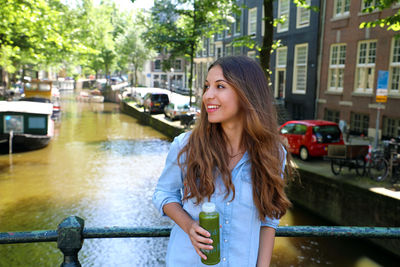 Young woman smiling while sitting on railing in canal