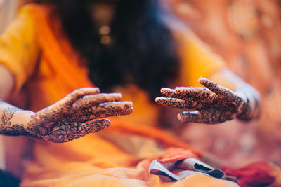 Midsection of woman with henna tattoo on hand sitting at home
