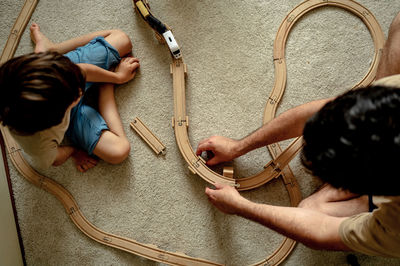 Dad and son are playing the train, they are building a railway from wooden blocks