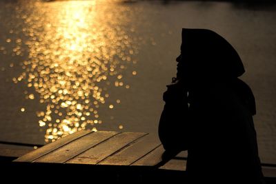 Side view of silhouette woman at table during sunset
