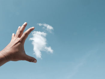 Cropped hand against blue sky