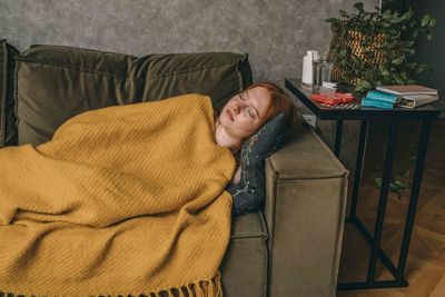Young woman in golden blanket, sleeping on cozy couch. scene  side table holding essentials