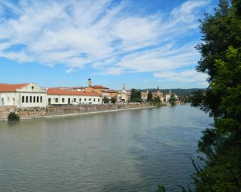 View of buildings by river against cloudy sky