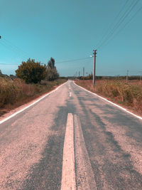 Road by electricity pylon against sky