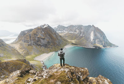 Rear view of man standing on cliff by sea at lofoten archipelago