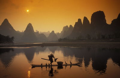Man sailing boat with birds in river against mountains