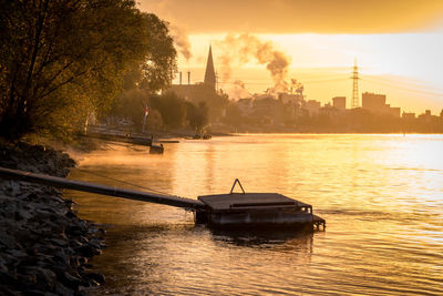 Boat in river by city against sky during sunset