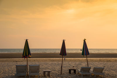 Lounge chairs and parasol at beach against sky during sunset
