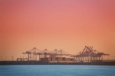 Cranes in sea against clear sky during sunset