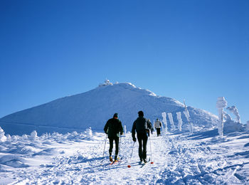 People on snow covered mountain against clear blue sky