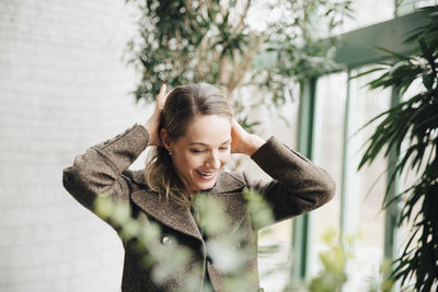 Smiling businesswoman tying hair while standing at office