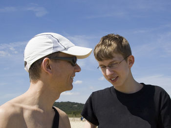 Close-up of happy man with son standing at beach against blue sky