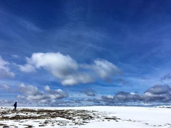 Person walking on snow covered field against sky